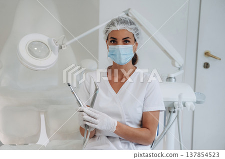 In protective mask. Podiatrist is in the clinic with equipment In protective mask. Podiatrist is in the clinic with equipment 137854523