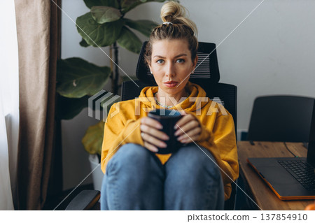 Serious woman holding coffee in home office showing emotional tension and mental overload in remote work isolation lifestyle 137854910