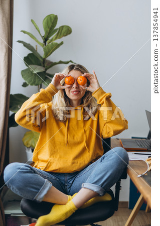 Playful woman holding tangerines over eyes having fun at home office with creative lifestyle and joyful mood in modern interior 137854941