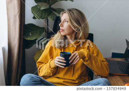 Freelancer woman taking break with coffee in home office looking aside reflecting on work life balance in remote lifestyle Freelancer woman taking break with coffee in home office looking aside reflecting on work life balance in remote lifestyle 137854949