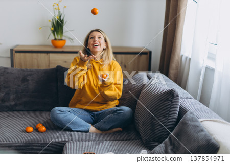 Happy woman tossing tangerines in air enjoying playful healthy lifestyle and joyful energy at home in cozy modern interior 137854971