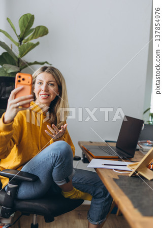 Female blogger recording video on smartphone during online call in home office with remote communication and digital content creation Female blogger recording video on smartphone during online call in home office with remote communication and digital content creation 137854976