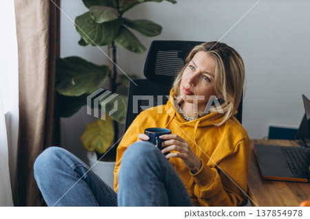 Pensive woman holding coffee reflecting in home office with quiet introspective mood and mental reset moment in soft daylight 137854978