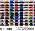Horizontal close-up photo with a dense display of colorful thread spools. Suitable for sewing, textile industry, tailoring, atelier and craft supply themes. 137855009