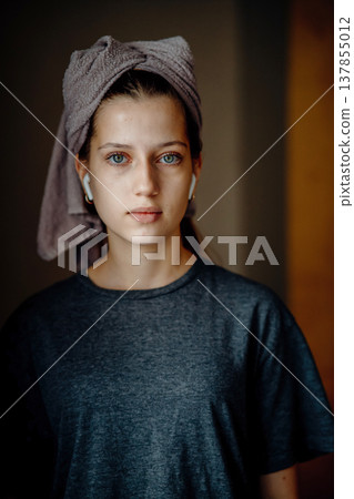 Natural portrait of a teen girl after a shower, with a towel on her head and earphones. Home lifestyle image for themes of morning routine, self care, natural skin and teenage everyday life. Natural portrait of a teen girl after a shower, with a towel on her head and earphones. Home lifestyle image for themes of morning routine, self care, natural skin and teenage everyday life. 137855012