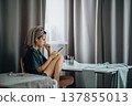 Teen girl sitting at a table with a smartphone, earphones and a towel on her head. Wider home shot with useful copy space for text, banners and editorial layouts. 137855013