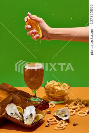 Lemon being squeezed above beer creating splash with oysters and snacks on bright background with copy space. Lemon being squeezed above beer creating splash with oysters and snacks on bright background with copy space. 137855096