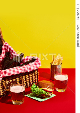 Burger with beer glasses and picnic basket on vibrant yellow and red background Burger with beer glasses and picnic basket on vibrant yellow and red background 137855105