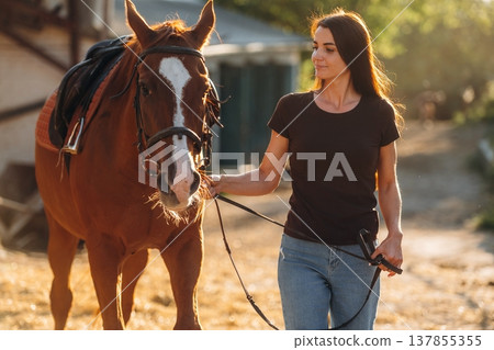 Black shirt and blue jeans. Woman is with horse on the farm 137855355