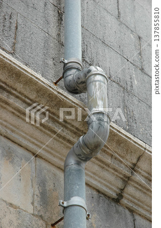 Vertical metal gutter pipe on an old stone facade 137855810