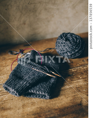 Hand knitted sock with needles and grey yarn ball on dark wooden background. Hand knitted sock with needles and grey yarn ball on dark wooden background. 137856539
