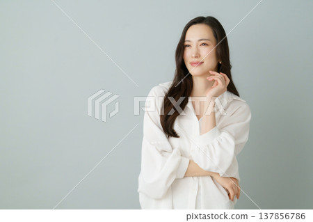 A portrait of a smiling young Japanese woman in a white shirt against a gray background. A portrait of a smiling young Japanese woman in a white shirt against a gray background. 137856786