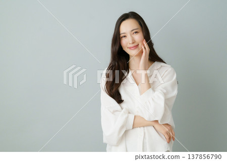 A portrait of a smiling young Japanese woman in a white shirt against a gray background. A portrait of a smiling young Japanese woman in a white shirt against a gray background. 137856790