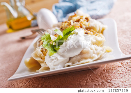 A plate with boiled dough vareniki with potato filling and fried onions. A plate with boiled dough vareniki with potato filling and fried onions. 137857359