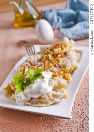 A plate with boiled dough vareniki with potato filling and fried onions. A plate with boiled dough vareniki with potato filling and fried onions. 137857360