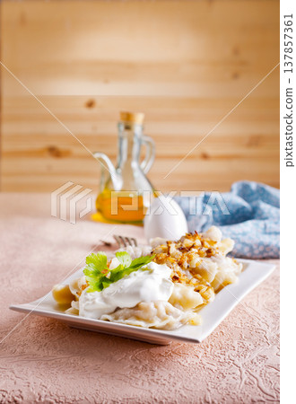 A plate with boiled dough vareniki with potato filling and fried onions. 137857361