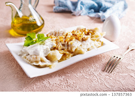 A plate with boiled dough vareniki with potato filling and fried onions. A plate with boiled dough vareniki with potato filling and fried onions. 137857363