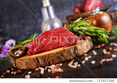 Seasoned raw beef steak with sea salt, cracked pepper, rosemary sprigs, and garlic cloves on black slate. Seasoned raw beef steak with sea salt, cracked pepper, rosemary sprigs, and garlic cloves on black slate. 137857386