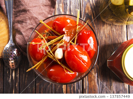Tasty pickled tomatoes in glass bowl, on wooden table, closeup 137857449