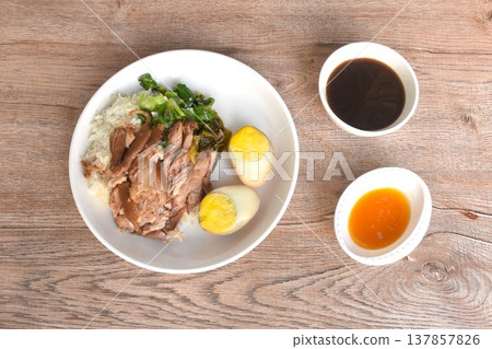 braised slice pork leg stew black Chinese herb soup topping brown boiled egg half cutting eat couple pickled cabbage and kale dipping  mixed spicy sour chili sauce on plain rice in white plate  137857826