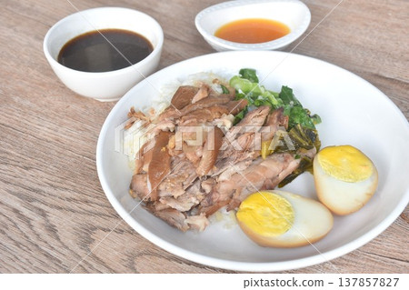 braised slice pork leg stew black Chinese herb soup topping brown boiled egg half cutting eat couple pickled cabbage and kale dipping  mixed spicy sour chili sauce on plain rice in white plate  137857827