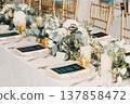 Wedding table decor in a white green gold palette with bouquet flowers, beautiful green glasses and a menu on a white tablecloth. The setting is decorated in bright colors and light pastel tones 137858472