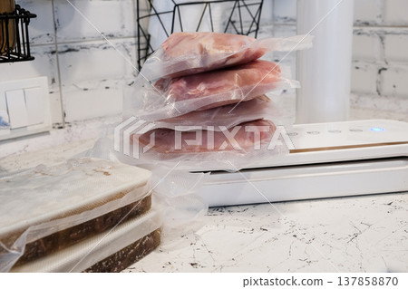 Home vacuum packer for food storage and freezing, canning products. Portions of vacuum-packed raw chicken breast, minced meat and frozen meat broth for cooking and souping. 137858870