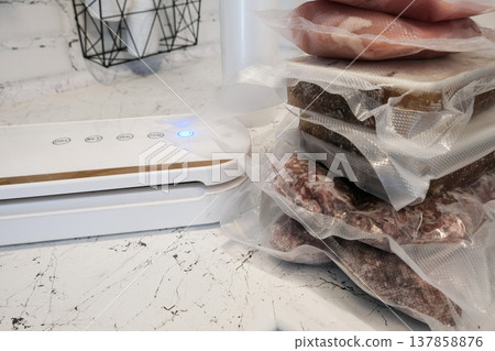 Home vacuum packer for food storage and freezing, canning products. Portions of vacuum-packed raw chicken breast, minced meat and frozen meat broth for cooking and souping. 137858876
