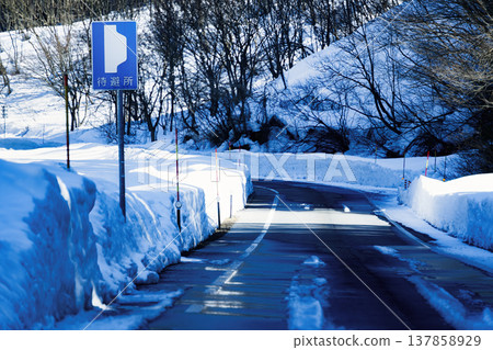 高聳的雪牆、避難所的標誌以及通往冬季山路的蜿蜒道路構成了一幅美麗的景象。 高聳的雪牆、避難所的標誌以及通往冬季山路的蜿蜒道路構成了一幅美麗的景象。 137858929