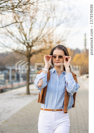 Elegant young woman in old money style holding sunglasses while standing on pier near Prague in early spring. Quiet luxury aesthetic and refined European elegance concept. Elegant young woman in old money style holding sunglasses while standing on pier near Prague in early spring. Quiet luxury aesthetic and refined European elegance concept. 137859086