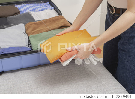 Weekend packing, open suitcase on the bed at home. Cropped female hands stack clothes and place Weekend packing, open suitcase on the bed at home. Cropped female hands stack clothes and place 137859491