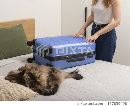 Young woman packing a blue hard shell suitcase on bed at home. Cozy travel preparation moment with a 137859498