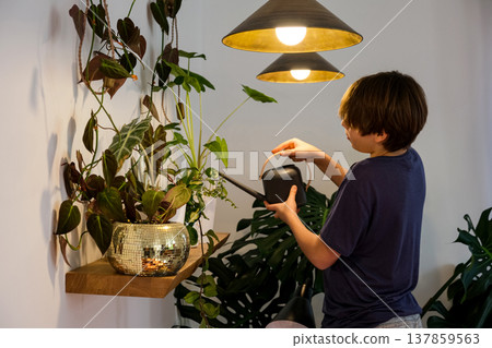 Teenage boy watering indoor plants at home, sustainable lifestyle and indoor gardening 137859563