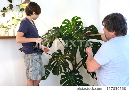 Father and teenage son caring for indoor plants at home, family bonding and sustainable lifestyle Father and teenage son caring for indoor plants at home, family bonding and sustainable lifestyle 137859568