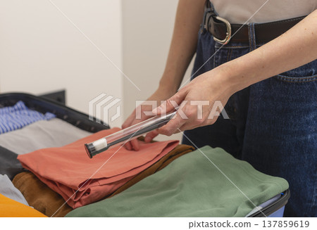 Hands placing a toothbrush in a protective case onto folded clothes inside an open suitcase. 137859619