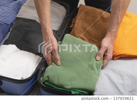 Hands placing neatly folded clothes into an open suitcase during packing at home. Close-up travel 137859621