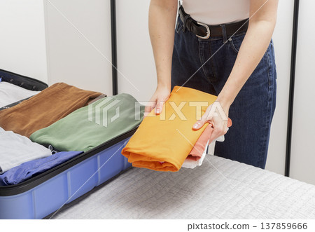 Packing into an open suitcase ready for travel. Cropped female hands fold clothes and place personal Packing into an open suitcase ready for travel. Cropped female hands fold clothes and place personal 137859666