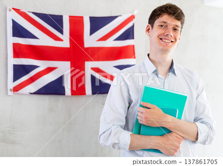 Male student with notebooks in his hands against background of the UK flag. Concept of studying abroad and immigration Male student with notebooks in his hands against background of the UK flag. Concept of studying abroad and immigration 137861705