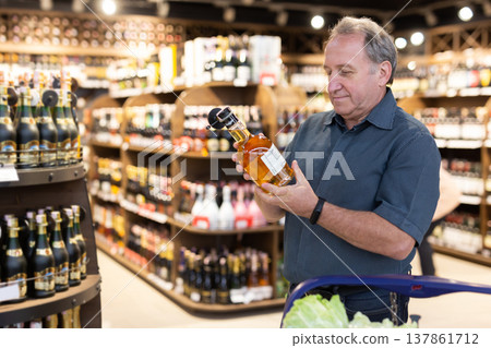Mature man choosing nice bottle of liquor in supermarket Mature man choosing nice bottle of liquor in supermarket 137861712