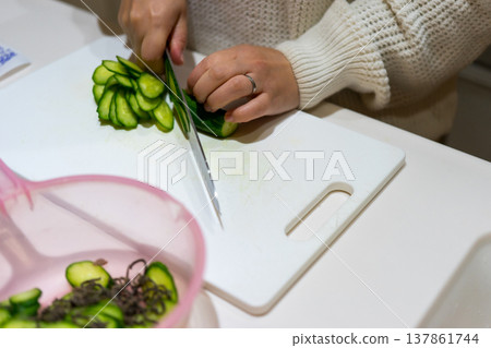 一位家庭主婦將黃瓜切成圓片。 一位家庭主婦將黃瓜切成圓片。 137861744