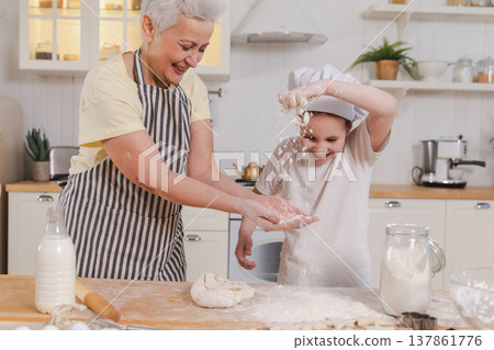 Happy family in kitchen. Grandmother and granddaughter child cook in kitchen together. Grandma teaching kid girl knead dough bake cookies. Household teamwork helping family generations concept Happy family in kitchen. Grandmother and granddaughter child cook in kitchen together. Grandma teaching kid girl knead dough bake cookies. Household teamwork helping family generations concept 137861776