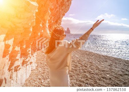 Woman beach freedom stands with her arms outstretched on a rocky pebble shore near a cliff during a bright golden sunset Woman beach freedom stands with her arms outstretched on a rocky pebble shore near a cliff during a bright golden sunset 137862538