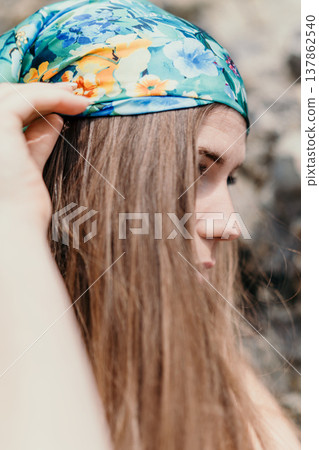 Woman scarf profile young lady adjusts her floral headscarf outdoors against a soft natural background during the summer Woman scarf profile young lady adjusts her floral headscarf outdoors against a soft natural background during the summer 137862540