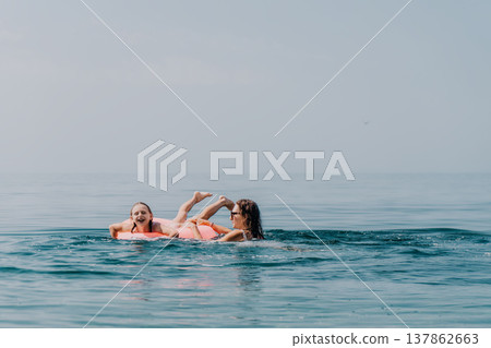 Mother girl swimming with pink inflatable ring during a summer beach vacation in the calm blue ocean water 137862663
