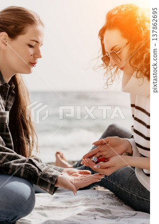 Women dice beach two young friends play a board game while sitting on a blanket at the seaside on a sunny summer day Women dice beach two young friends play a board game while sitting on a blanket at the seaside on a sunny summer day 137862695