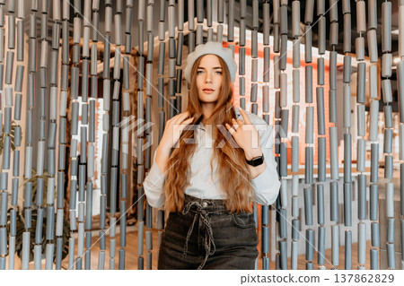 Woman beret fashion posing behind a decorative cylinder bead curtain in a light blue shirt and trendy dark jeans 137862829
