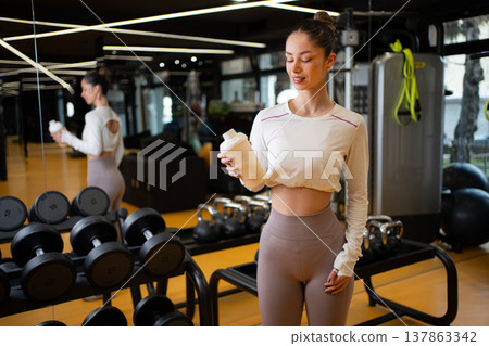 Young woman holding protein shaker bottle in health club Young woman holding protein shaker bottle in health club 137863342
