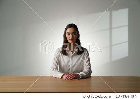a young girl in a white shirt sits at a table in the office, holds a pen in her hands 137863494