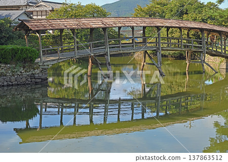 A covered bridge in the Ishidatami district of Uchiko town, Ehime Prefecture. The beautiful wooden structure and the tranquil mountain village scenery are reflected on the surface of the pond. A covered bridge in the Ishidatami district of Uchiko town, Ehime Prefecture. The beautiful wooden structure and the tranquil mountain village scenery are reflected on the surface of the pond. 137863512