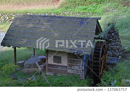 A watermill standing in Ishidatami Seiryuen, Uchiko Town, Ehime Prefecture. A mountain village landscape with a moss-covered cedar bark roof and a traditional wooden watermill. A watermill standing in Ishidatami Seiryuen, Uchiko Town, Ehime Prefecture. A mountain village landscape with a moss-covered cedar bark roof and a traditional wooden watermill. 137863757